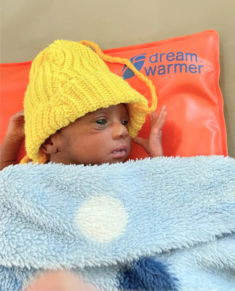 Infant on a DreamWarmer warming mattress covered with a blanket and hat.