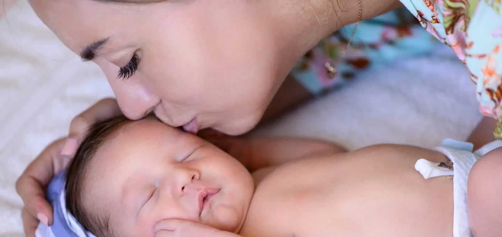 A mother kissing a newborn child on the forehead.
